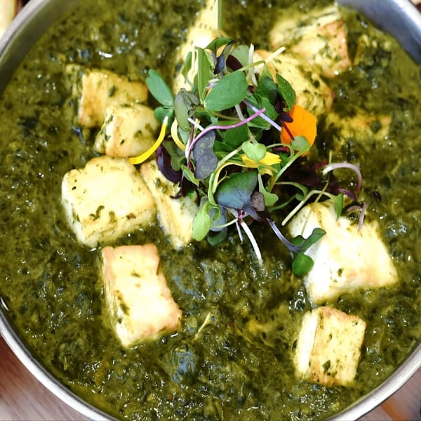 Close-up of Everest Indian Cuisine's Palak Paneer, a vibrant green spinach curry with paneer cheese cubes and microgreens.