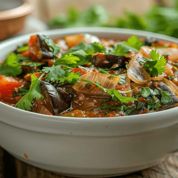 Close-up of an Indian eggplant and onion curry, garnished with fresh cilantro in a white bowl.