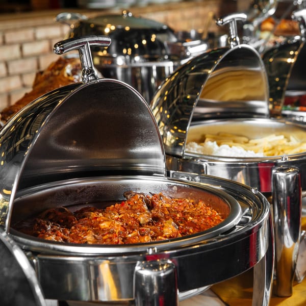 Indian buffet with a chafing dish of chicken curry and another with rice and fries.