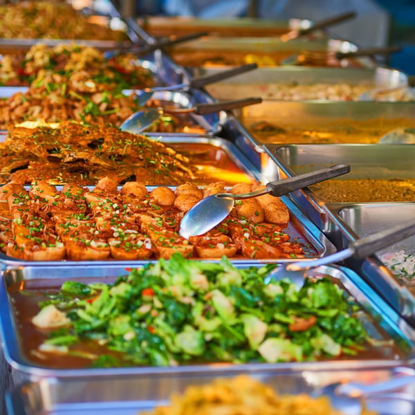 A buffet spread of various Indian dishes in metal trays, including curries and vegetables.