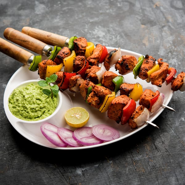 Three skewers of Everest Indian Cuisine's chicken tikka with bell peppers and onions, served with green chutney.